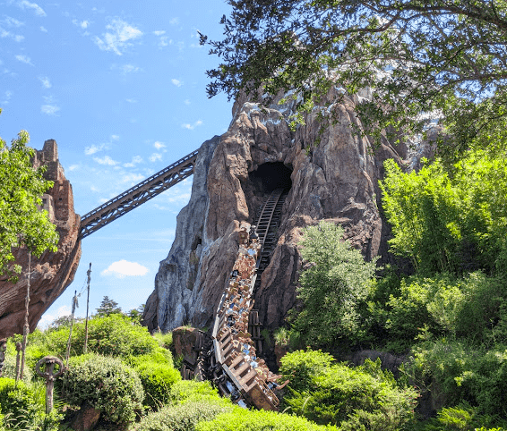 View of a full-ride vehicle coming out of the mountain and down the steepest drop on Expedition Everest at Animal Kingdom. Initial sharp incline visible in background.