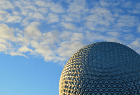 Partial shot of EPCOT’s Spaceship Earth during golden hour with a blue sky with scattered clouds in the background.