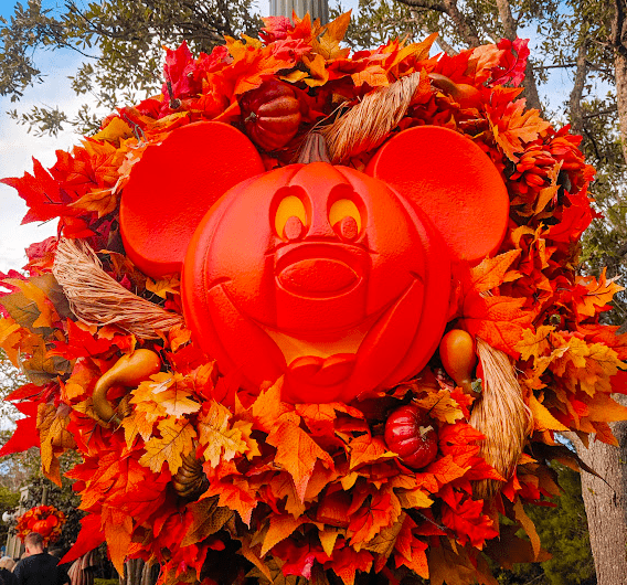 Mickey pumpkin head in a wreath of red, yellow, and orange leaves, sunflowers, and tiny fall accents on a lamppost in Magic Kingdom.