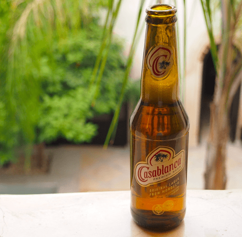 Amber colored bottle of Casablanca Beer on a ledge with lush tropical plants in the background.