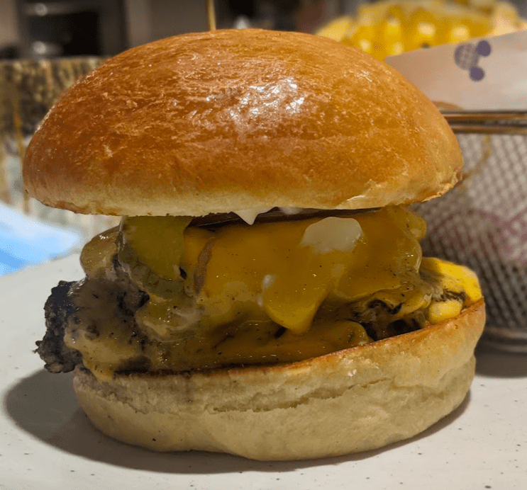 Close-up of Steakhouse 71 Stack Burger on a plate showcasing the melted American cheese and blended beef patty on a brioche bun. 