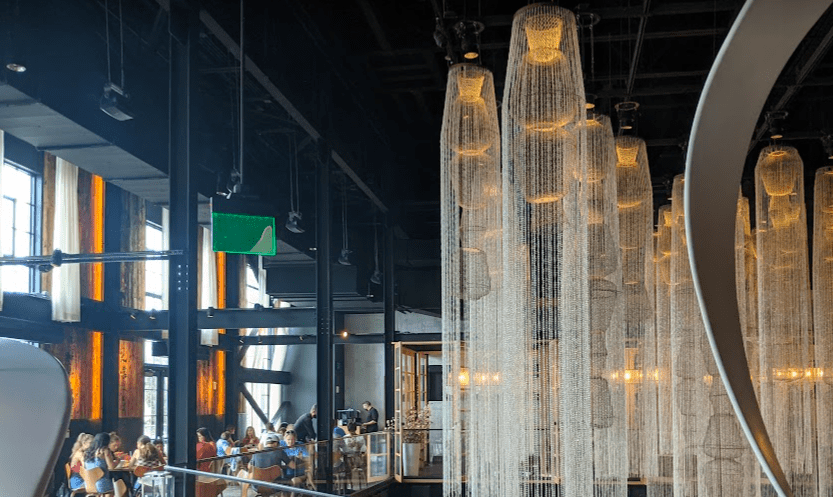 Taken from the second level of Morimoto at Disney Springs, photo showcases the famous 20-foot-long chandeliers as well as a catwalk with glass walls overlooking the first floor dining room.
