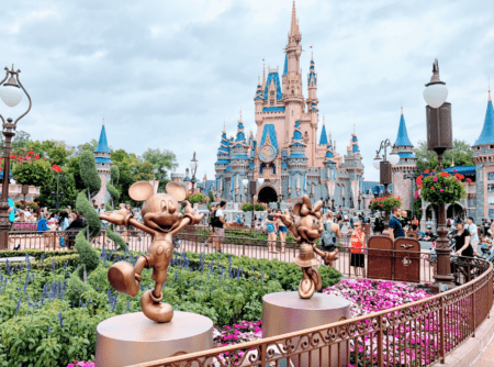 Mickey Mouse and Minnie Mouse Fab 50 statues surrounded by flowers with Cinderella Castle in the background.