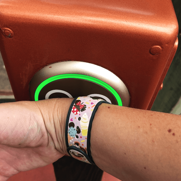 Person using their pink Disney-snack-themed MagicBand to scan into a Disney World park touch point.