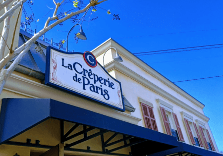 Photo of the outside of La Creperie de Paris restaurant at Disney World's EPCOT against a blue sky.