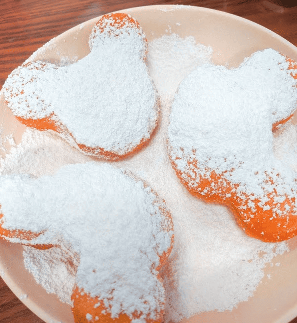 Three Mickey Mouse shaped beignets on a plate covered in powered sugar.