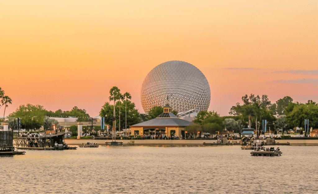 A view of the EPCOT Ball from across the lake with a colorful sunset background.