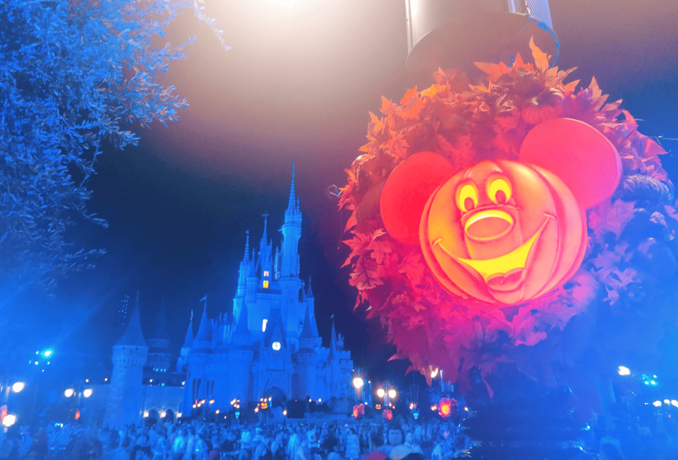 A decorative orange Mickey Mouse Pumpkin hanging in front of a darkly lit Cinderella Castle.