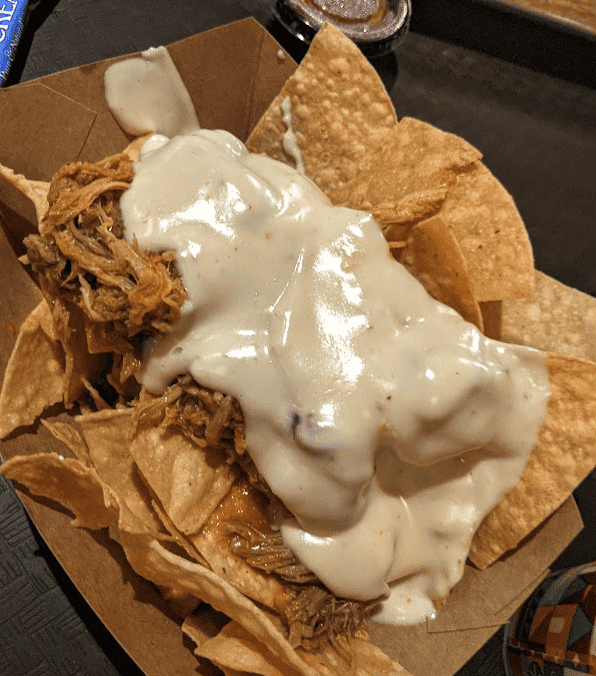 Tortilla chips in a paper bowl topped with pulled pork and melted queso cheese.