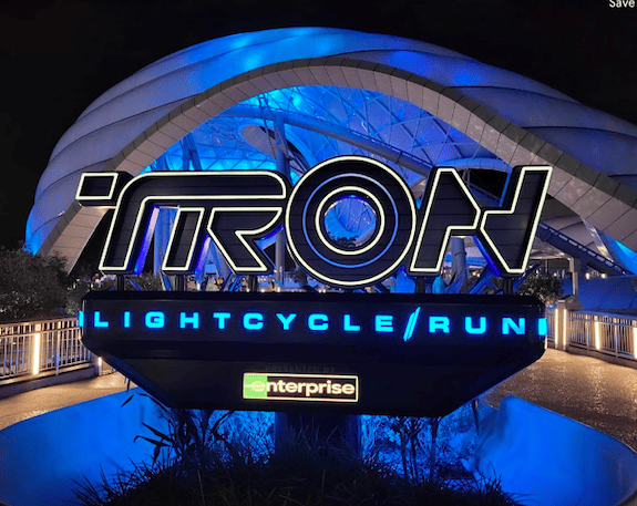 Illuminated TRON Lightcycle Run sign at night with TRON pavilion in background.