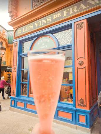 A bubbly flute of champagne held up in front of the Les Vins de France storefront in EPCOT.