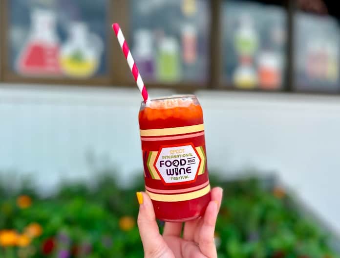 Someone holding a full drink with the EPCOT Food & Wine Festival logo and a red and white striped straw