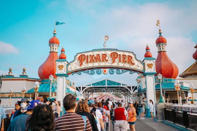 Pixar Pier entrance with two red tiers and turquoise details with crowd of people walking in